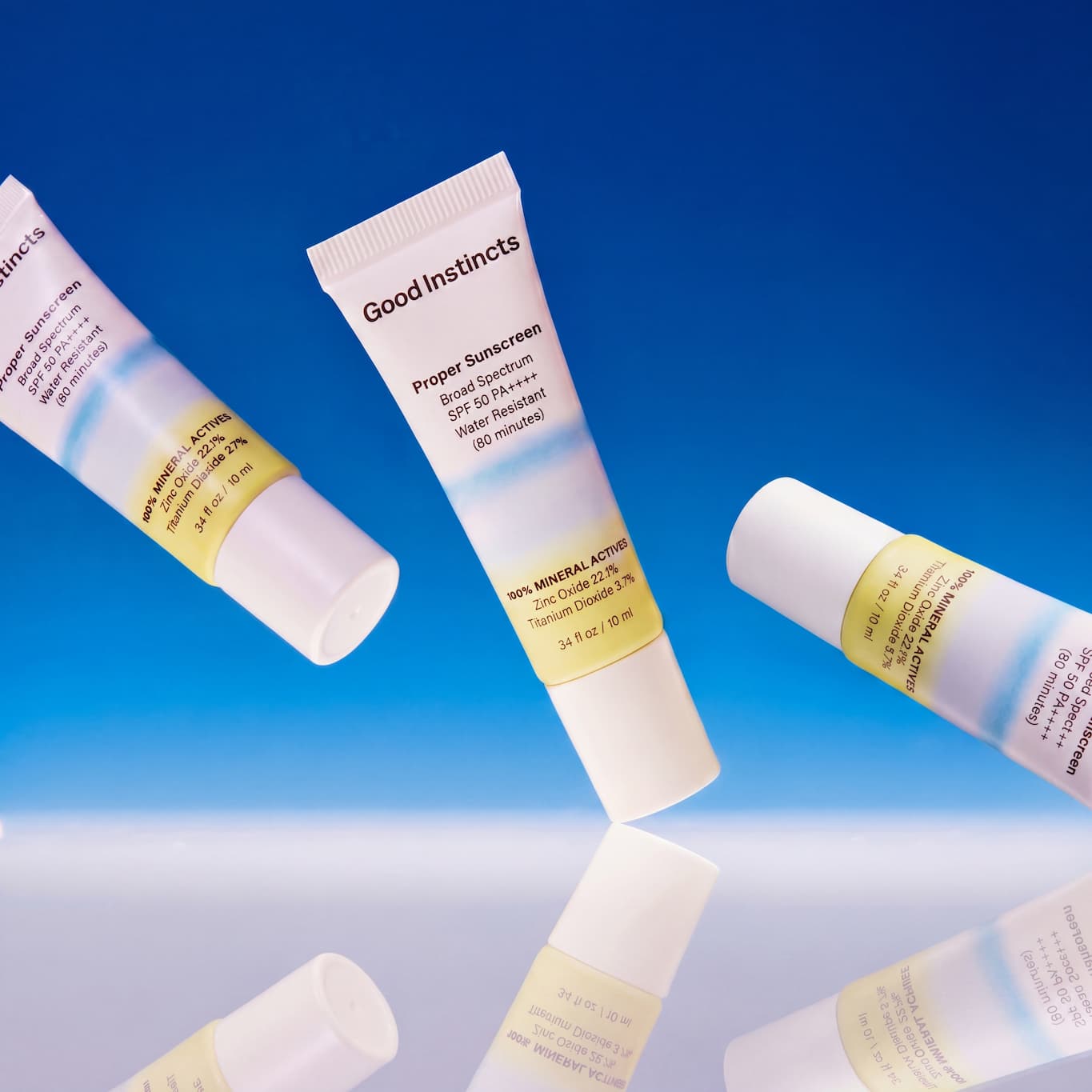 Good Instincts sunscreen tubes on a reflective surface with a blue gradient background