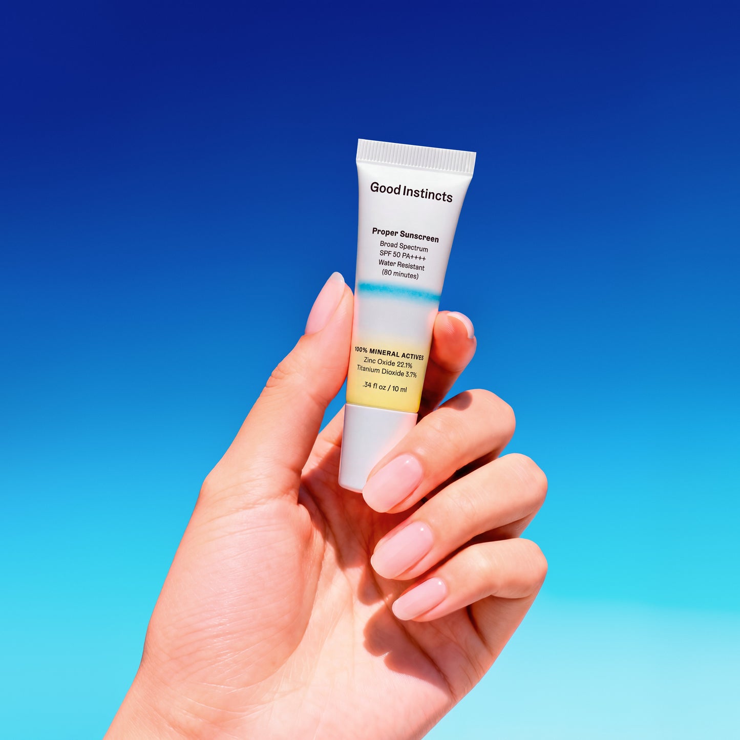 Hand holding a tube of Good Instincts sunscreen against a blue sky background