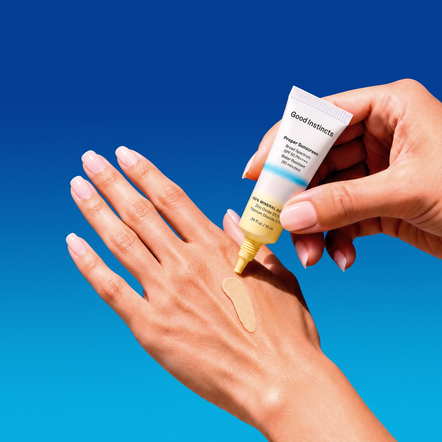 Hand applying sunscreen to another hand with a blue background