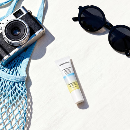 Camera, sunglasses, and sunscreen on a white surface